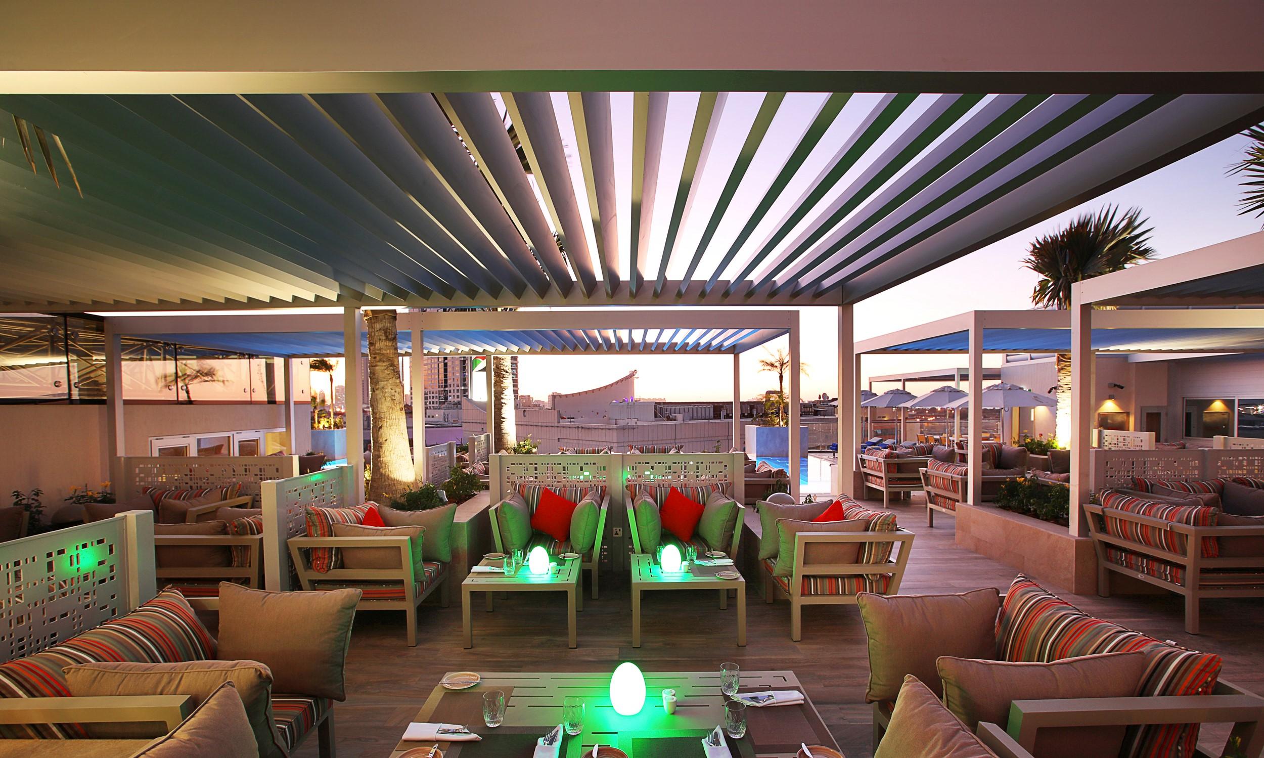 Grand Cosmopolitan Hotel Dubai Exterior foto The photo depicts a stylish outdoor lounge area, likely located on a rooftop or terrace. The space features modern furnishings with comfortable seating, including sofas and tables. There are colorful cushions accenting the seating, and some tables ha
