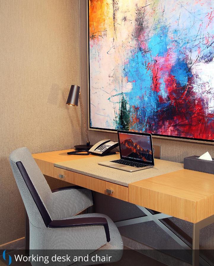 Grand Cosmopolitan Hotel Dubai Exterior foto The photo depicts a modern workspace. There's a wooden desk with a sleek design, equipped with a laptop open on the surface. Next to the laptop, there is a classic telephone and a small box of tissues. A stylish lamp is positioned on the desk for lig
