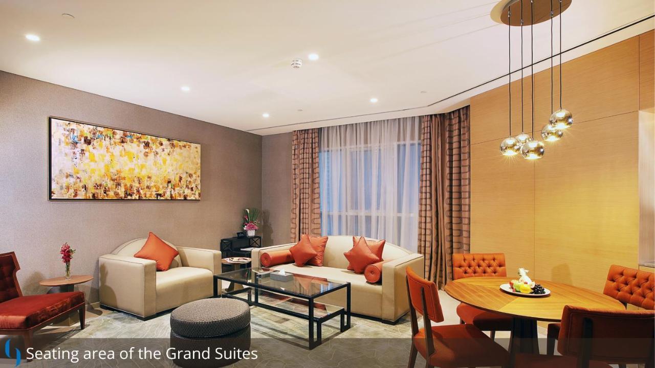 Grand Cosmopolitan Hotel Dubai Exterior foto The photo depicts a stylish and modern living area within a suite. There is a light-colored sofa with decorative cushions, a glass coffee table in the center, and a cozy armchair nearby. To the side, there is a small round dining table with four chai